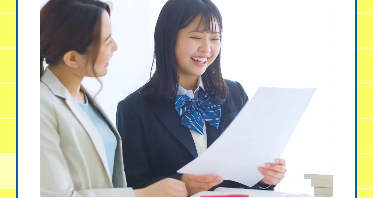講師と一緒にプリントを見ながら笑顔で学ぶ女子高校生